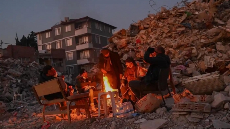 Locuitorii din Hatay, Turcia, ai căror apropiați sunt încă sub dărâmături se adună în jurul unui foc de tabără lângă clădirile prăbușite